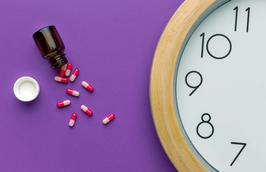 Foto van een half afgebeelde klok en een omgevallen potje met rode/roze capsules op een paarse ondergrond (Flatlay) (via Freepik)